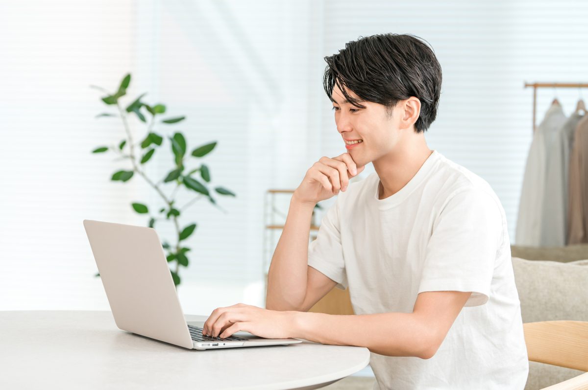自宅でノートPCに向かい笑顔を見せる男性